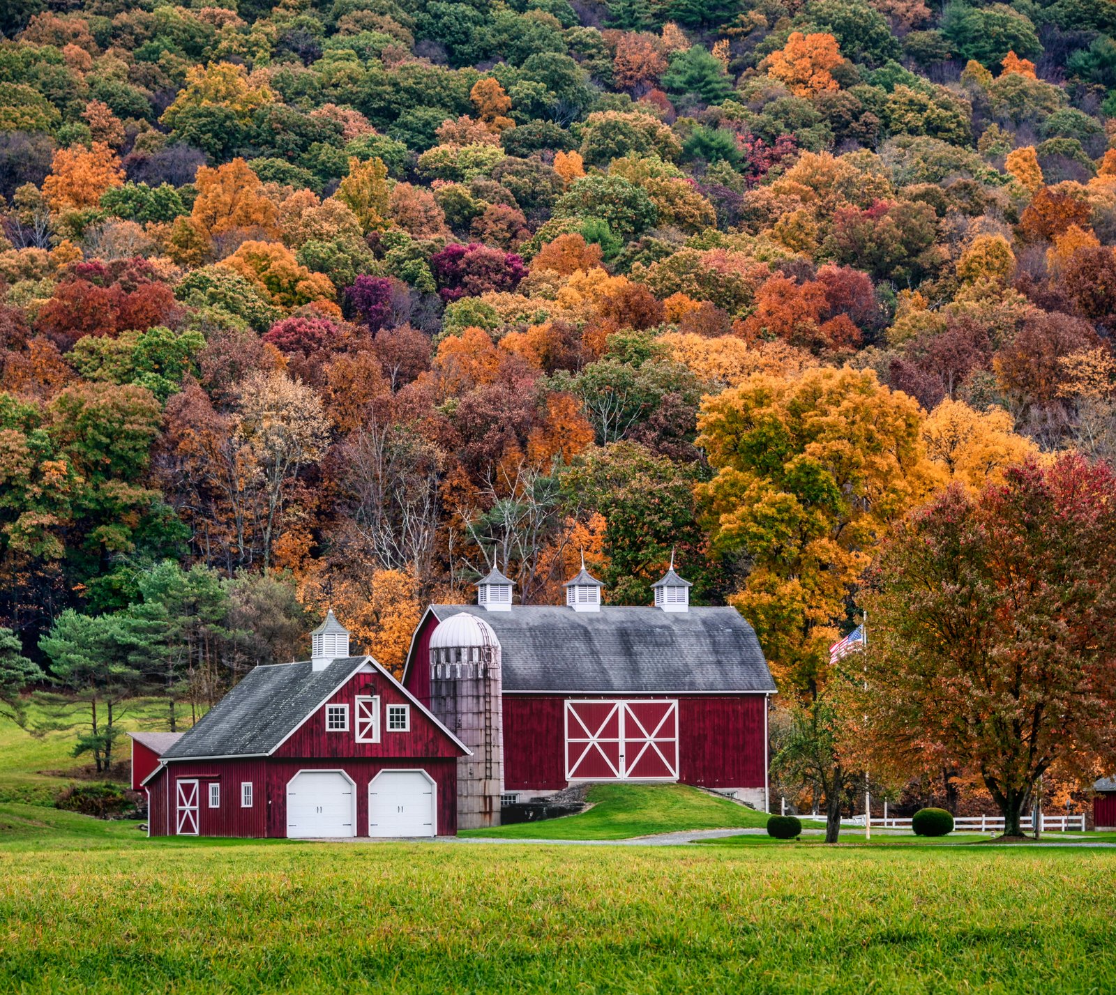 A red barn and home sitting before an autum landscape.